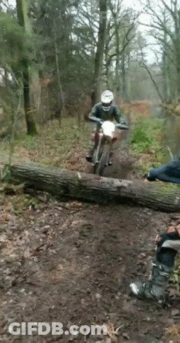 A Man On A Dirt Bike Is Riding Over A Log GIF