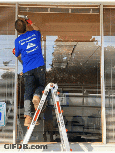 A Man On A Ladder Wearing A Blue Shirt That Says ' In Glass Install Llc ' GIF