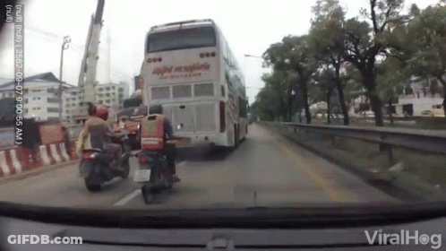 A Man On A Motorcycle Is Standing In Front Of A Double Decker Bus . GIF