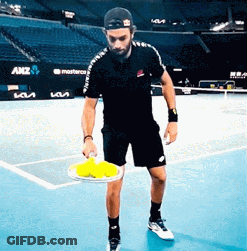 A Man On A Tennis Court Holding A Tennis Racquet And Balls GIF