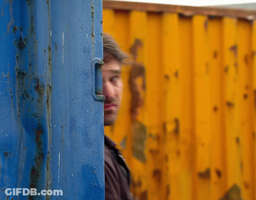 A Man Peeking Out From Behind A Blue And Yellow Wall GIF