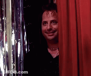 A Man Peeking Out From Behind A Red Curtain And Smiling GIF