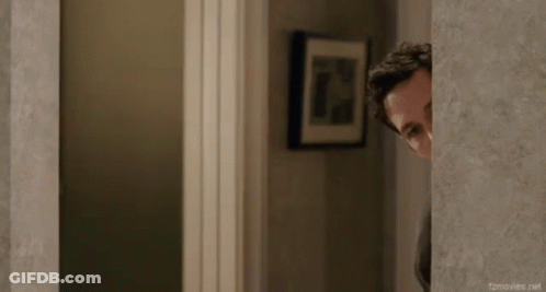 A Man Peeking Out From Behind A Wall In A Hallway . GIF