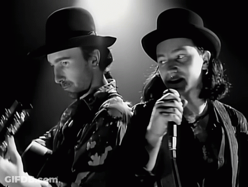 A Man Playing A Guitar And A Man Singing Into A Microphone In A Black And White Photo GIF