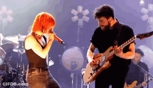 A Man Playing A Guitar And A Woman Singing Into A Microphone GIF