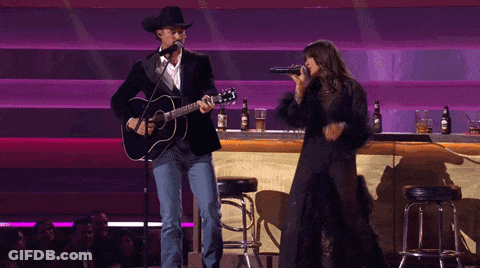 A Man Playing A Guitar And A Woman Singing Into A Microphone On A Stage GIF