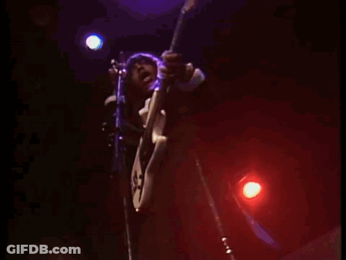A Man Playing A Guitar And Singing Into A Microphone On A Stage GIF