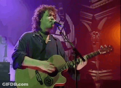 A Man Playing A Guitar And Singing Into A Microphone GIF