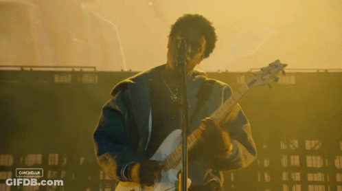 A Man Playing A Guitar And Singing Into A Microphone With A Sign That Says Canchella On The Bottom Right GIF