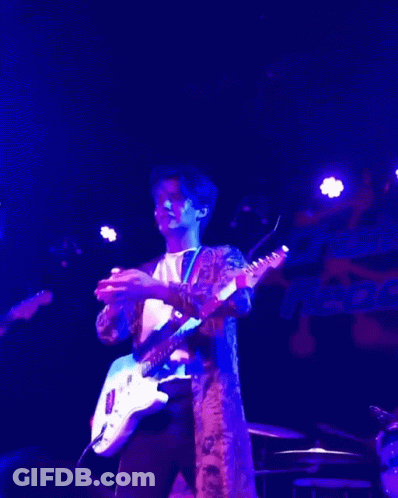 A Man Playing A Guitar In A Dark Room With Purple Lights GIF