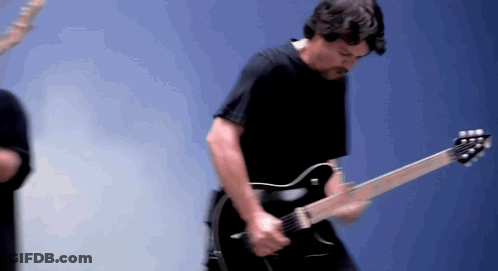 A Man Playing A Guitar In Front Of A Blue Wall GIF