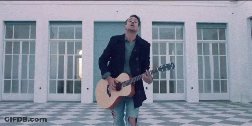 A Man Playing A Guitar In Front Of A Building GIF