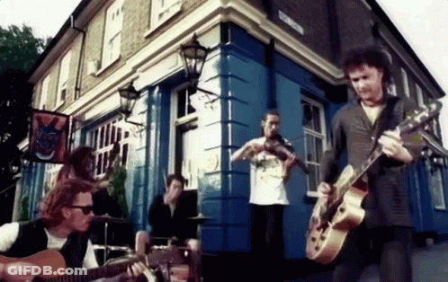 A Man Playing A Guitar In Front Of A Building With A Sign On It That Says ' A ' On It GIF