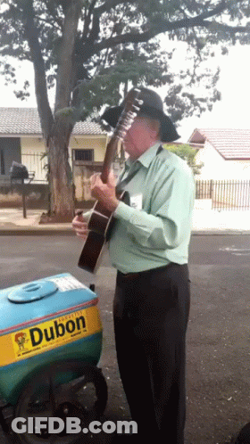 A Man Playing A Guitar In Front Of A Dubon Ice Cream Cart GIF