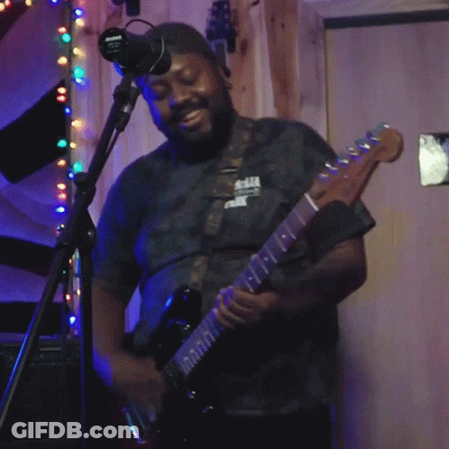 A Man Playing A Guitar In Front Of A Microphone With A Sign On The Wall That Says No Smoking GIF