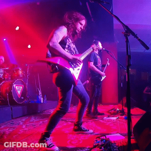 A Man Playing A Guitar In Front Of A Microphone With A Triangle On The Drum Set GIF
