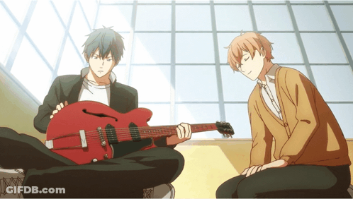 A Man Playing A Guitar Next To Another Man Sitting On The Floor GIF