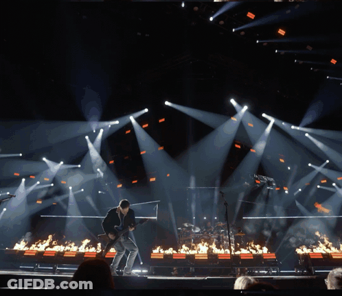 A Man Playing A Guitar On A Stage Surrounded By Fire GIF