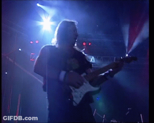 A Man Playing A Guitar On A Stage With A Blue Light Behind Him GIF