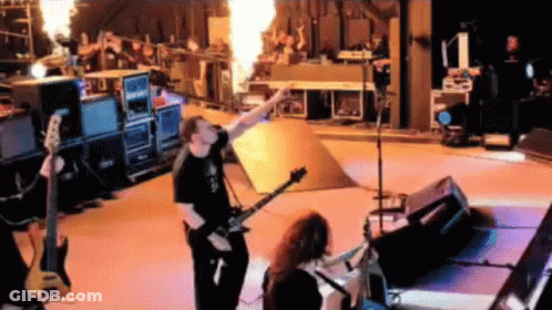 A Man Playing A Guitar On A Stage With Flames Coming Out Of It . GIF
