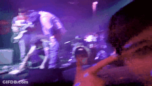 A Man Playing A Guitar On A Stage With Purple Lights GIF