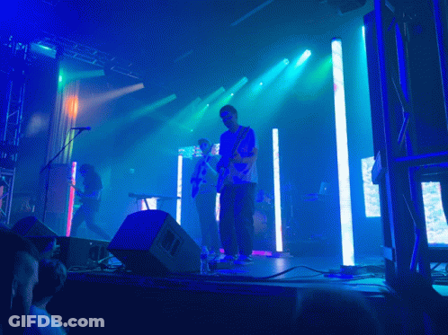 A Man Playing A Guitar On Stage With A Crowd Watching GIF