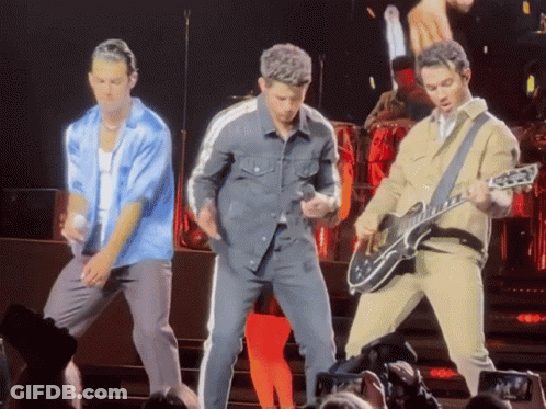 A Man Playing A Guitar On Stage With Two Other Men GIF