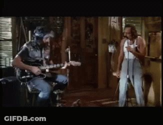 A Man Playing A Guitar While Another Man Sings Into A Microphone GIF