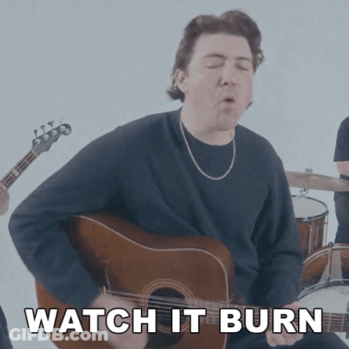 A Man Playing A Guitar With The Words " Watch It Burn " Behind Him GIF