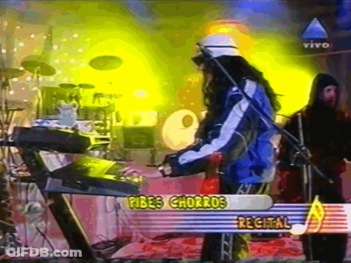 A Man Playing A Keyboard In Front Of A Sign That Says " Pibes Charros Recital " GIF