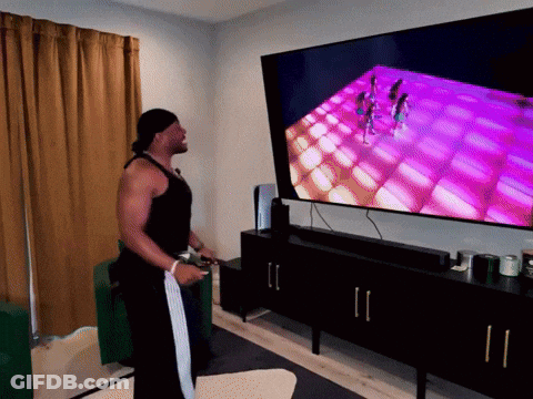 A Man Playing A Video Game In Front Of A Large Flat Screen Tv GIF