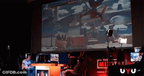 A Man Playing A Video Game On A Large Screen With A Sign That Says The Mix GIF
