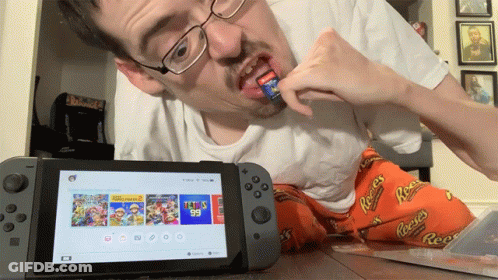 A Man Playing A Video Game On A Nintendo Switch While Wearing Reeses Pajamas GIF