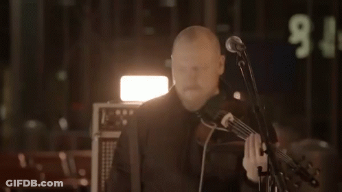 A Man Playing A Violin In Front Of A Microphone With The Number 9 On The Wall Behind Him GIF