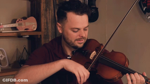 A Man Playing A Violin In Front Of A Shelf With A Pink Guitar That Says ' Elvis ' On It GIF
