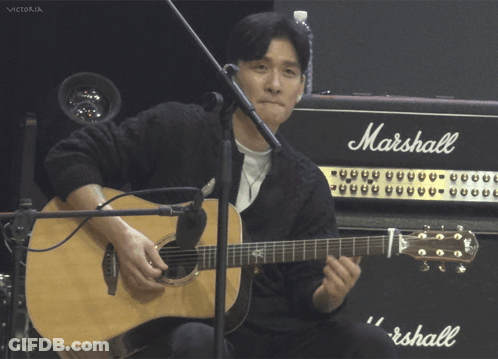 A Man Playing An Acoustic Guitar In Front Of A Marshall Amp GIF