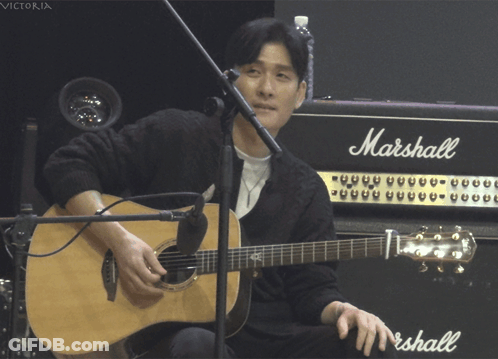 A Man Playing An Acoustic Guitar In Front Of A Marshall Amp GIF