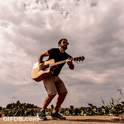 A Man Playing An Acoustic Guitar On A Dirt Road GIF