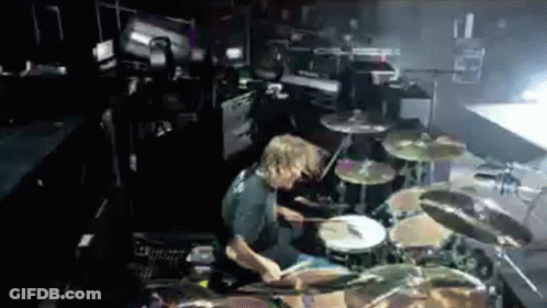 A Man Playing Drums In A Dark Room With A Drum Set GIF
