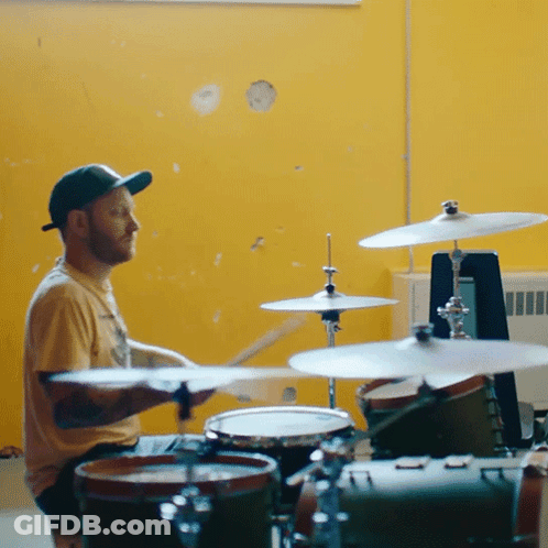A Man Playing Drums With A Yellow Wall Behind Him GIF