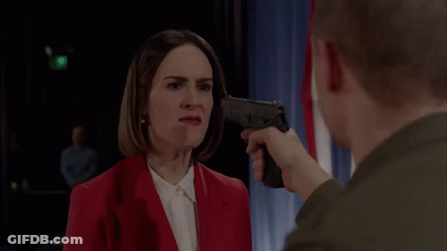 A Man Pointing A Gun At A Woman In A Red Jacket GIF