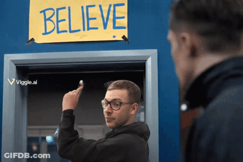 A Man Points To A Sign That Says Believe On It GIF