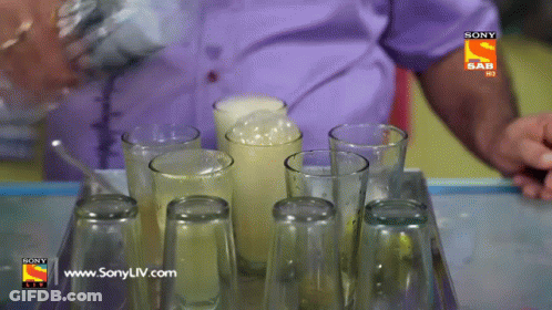 A Man Pouring A Drink Into A Tray Of Empty Glasses With A Sony Logo On The Bottom GIF