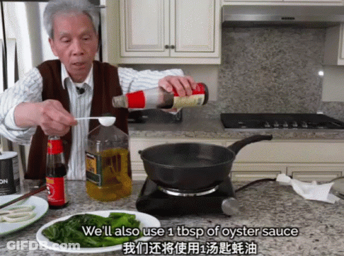 A Man Pouring Oyster Sauce Into A Frying Pan In A Kitchen GIF