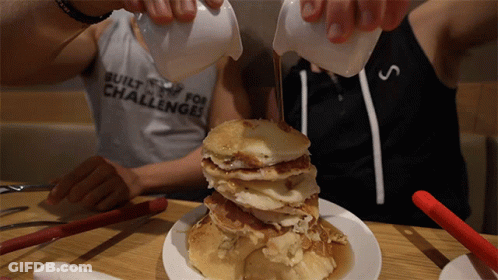 A Man Pouring Syrup On A Stack Of Pancakes With A Shirt That Says Built For Challenges GIF