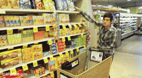 A Man Pushes A Shopping Cart Through A Grocery Store Aisle GIF