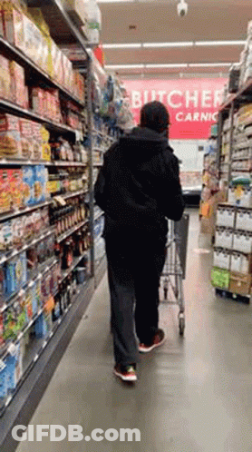 A Man Pushing A Shopping Cart In A Grocery Store With A Sign That Says Butcher Carnic GIF