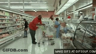 A Man Pushing A Shopping Cart Through A Grocery Store Aisle . GIF