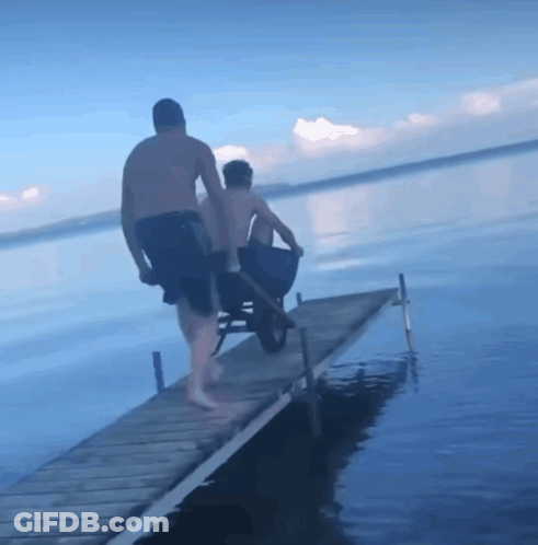 A Man Pushing Another Man In A Wheelbarrow Down A Pier GIF