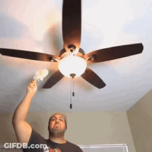 A Man Reaches Up To A Ceiling Fan While Wearing A Hat GIF